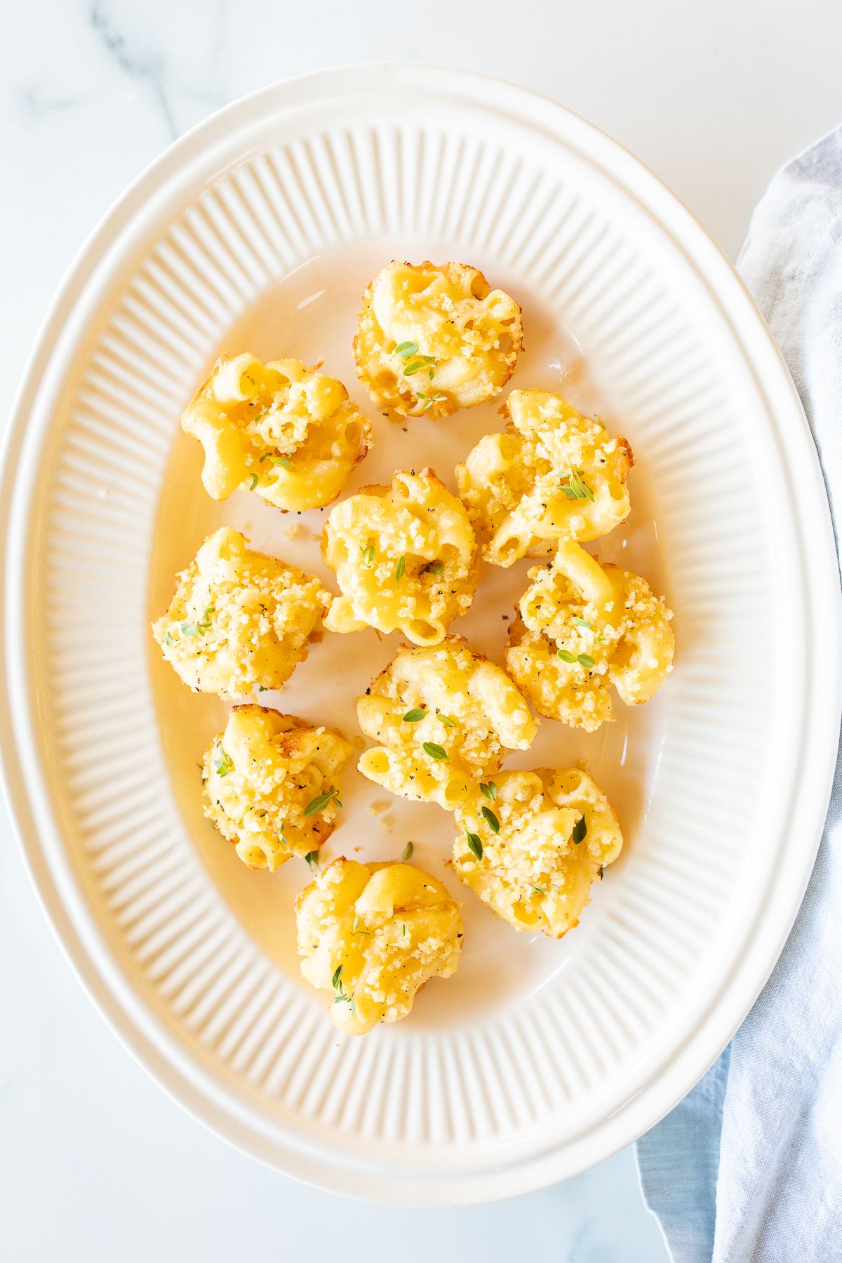 A white oval platter full of mini mac and cheese cups for an appetizer.