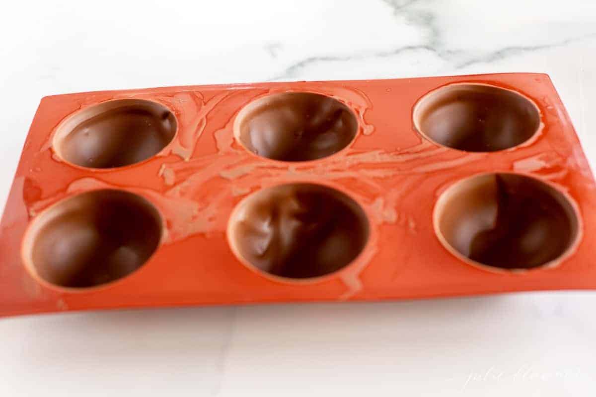 A red silicone sphere mold filled with chocolate for Mexican hot chocolate bombs.