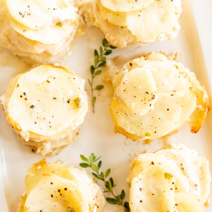 A white platter featuring potato gratin stacks, garnished with fresh thyme.