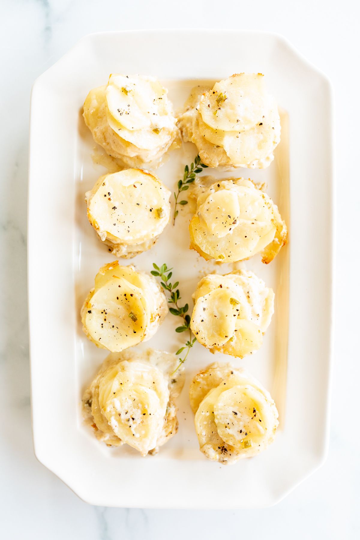 A white platter featuring potato gratin stacks, garnished with fresh thyme.