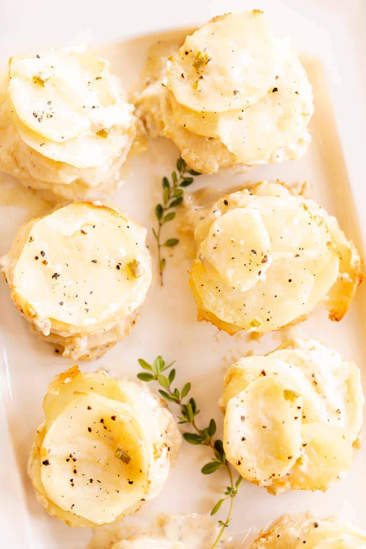 Individual stacks of potatoes au gratin on a white platter with touches of fresh thyme for garnish for a Thanksgiving recipe