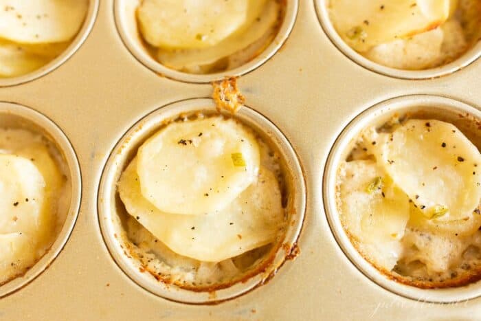 Potato gratin stacks in a gold muffin pan for individual servings.