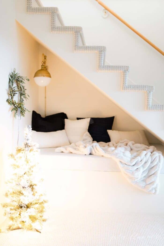 A built in nook under stairs, decorated for Scandinavian Christmas with a fresh wreath and a frosted Christmas tree.