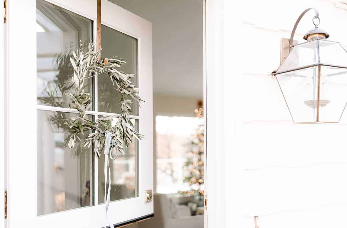 dutch door open with olive wreath peeking into a home with a scandinavian christmas tree