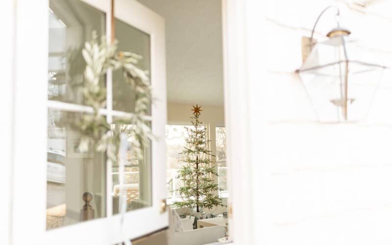 A white front porch with a natural christmas decor wreath on the dutch door.
