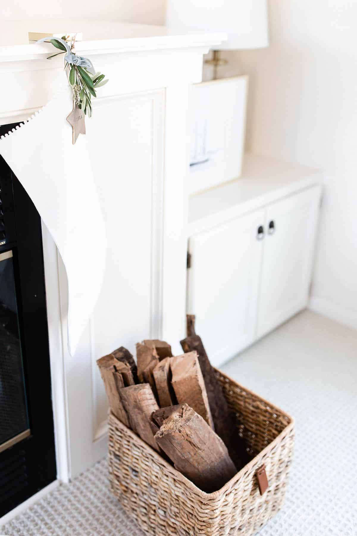 A white linen stocking hanging on a fireplace with a basket full of wood in front.