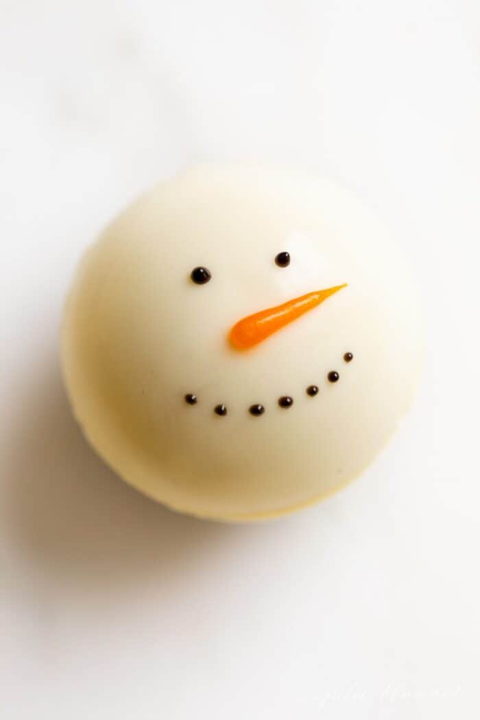 A snowman hot chocolate bomb on a white plate.