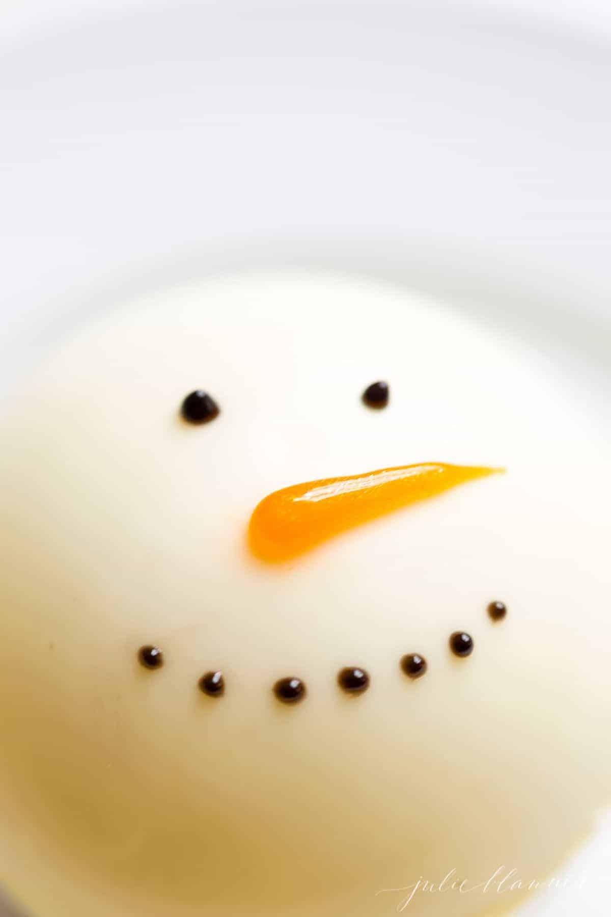 A Christmas hot chocolate bomb snowman on a white plate.