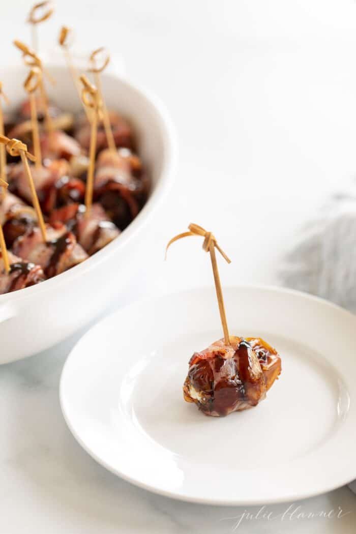 An individual stuffed date with a toothpick on a white plate, baking dish in background.