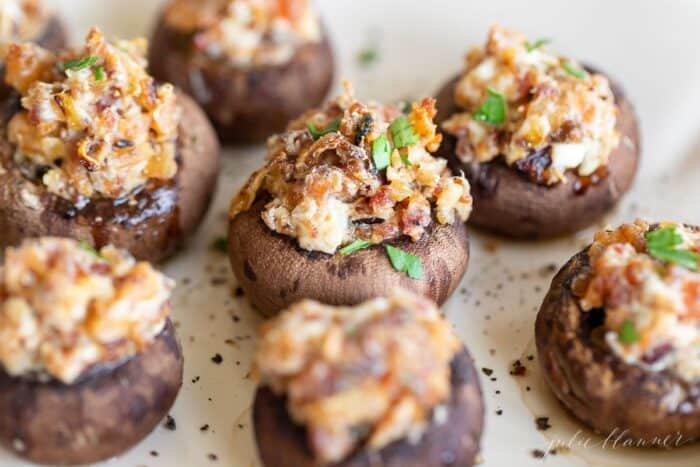 A white platter full of stuffed mushroom hors d'oeuvres on a white surface.