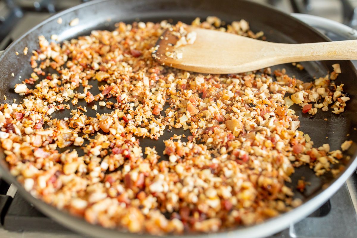 crumbled bacon, onions and mushroom pieces in a frying pan for a stuffed mushroom recipe