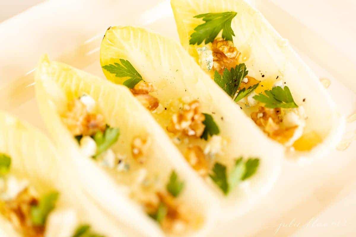 A healthy Thanksgiving appetizer image, a white platter with endive lettuce salad appetizers topped with nuts, cheese and parsley