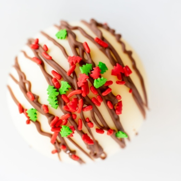 A white chocolate hot chocolate bomb, covered in red and green sprinkles.