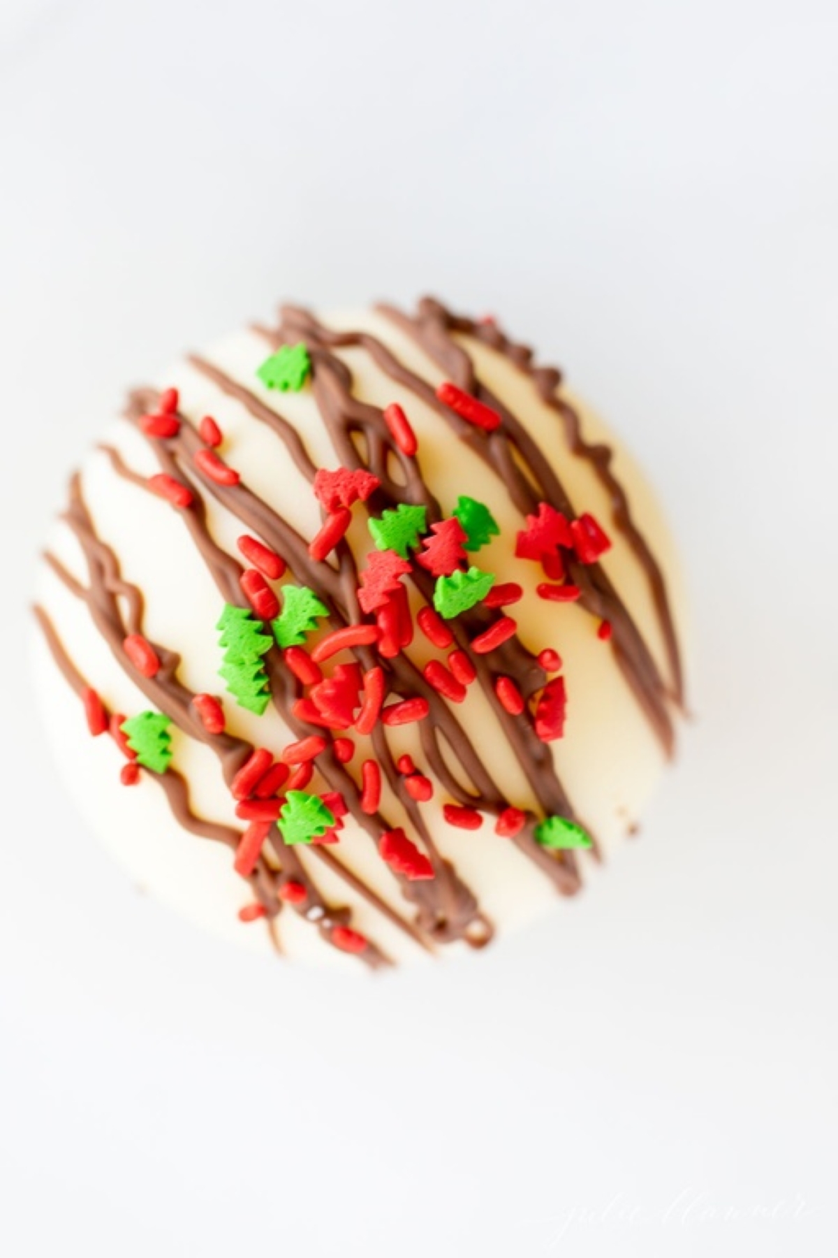 A white chocolate hot chocolate bomb, covered in red and green sprinkles.