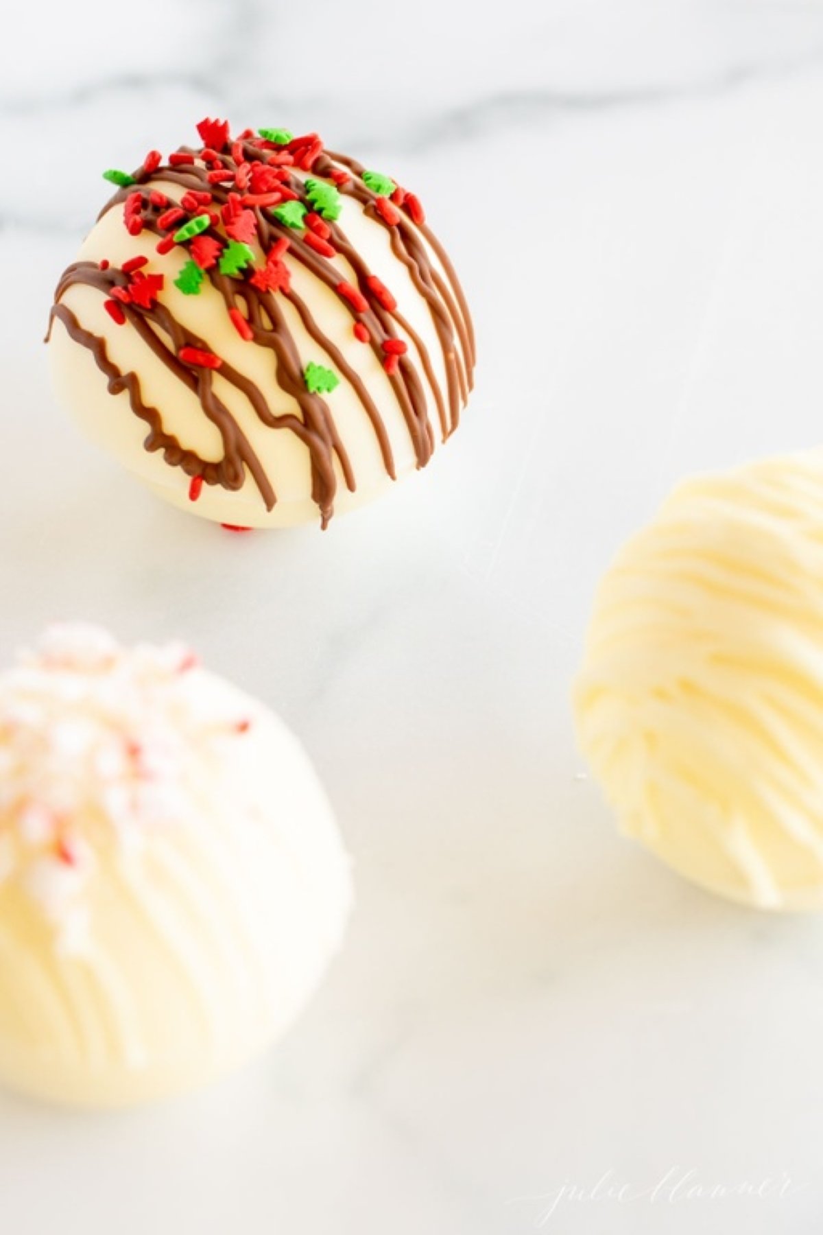 Three white chocolate hot cocoa bombs on a white marble countertop