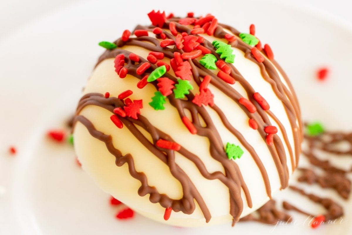 A white chocolate hot chocolate bomb, covered in red and green sprinkles.
