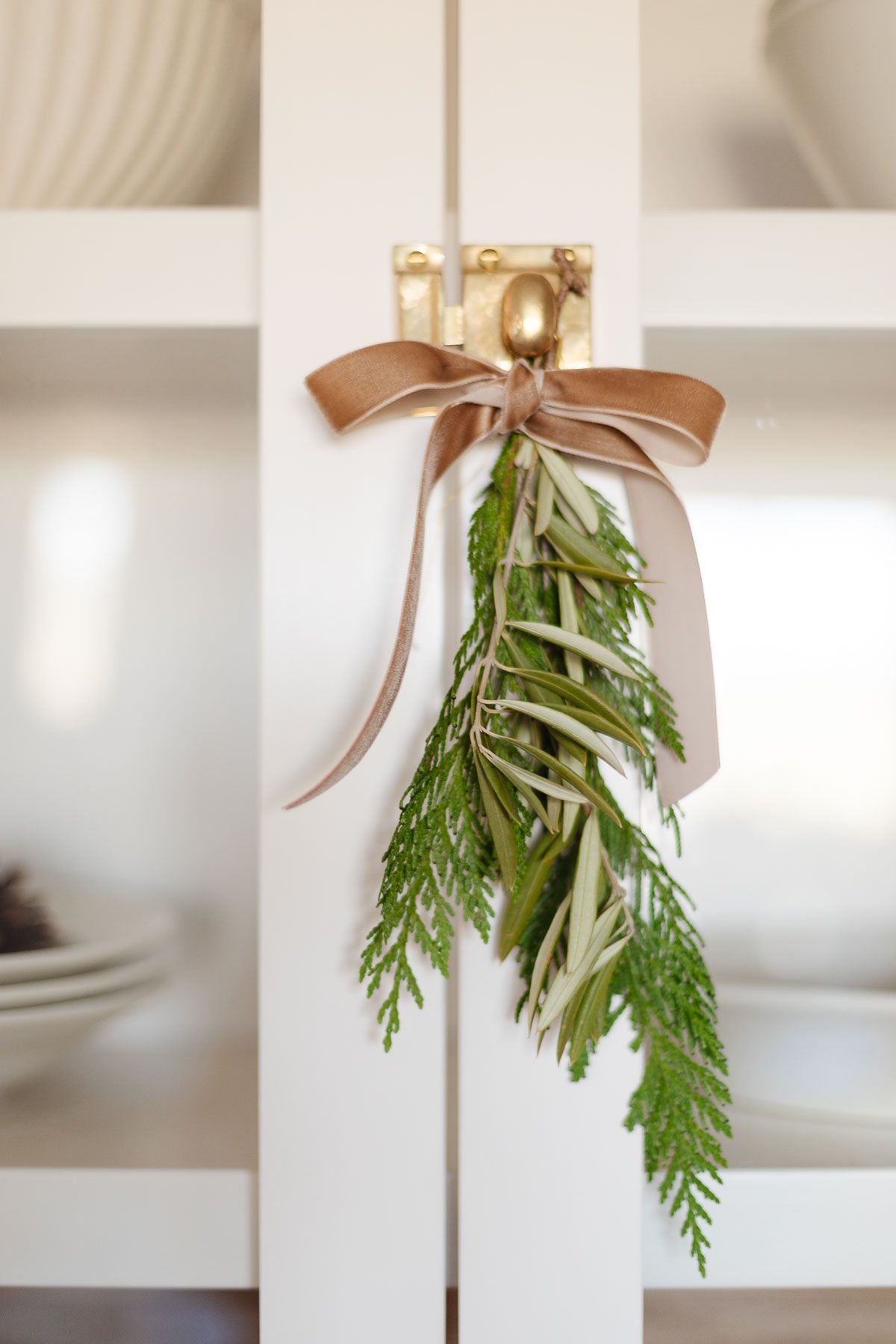 Fresh Christmas greenery tied with a bow onto a brass cabinet pull.