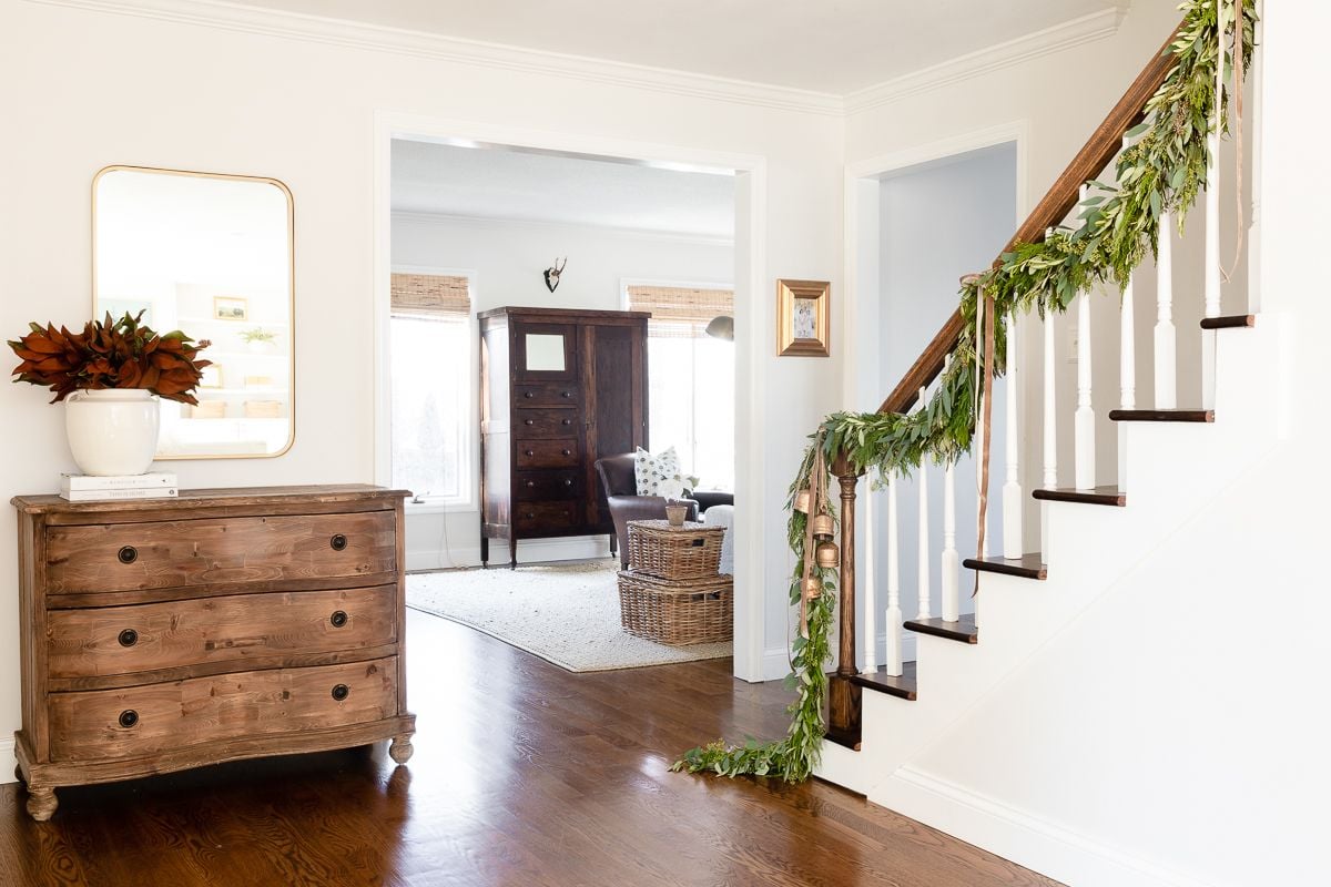 Fresh Christmas garlands on a staircase in a white entryway of a home.
