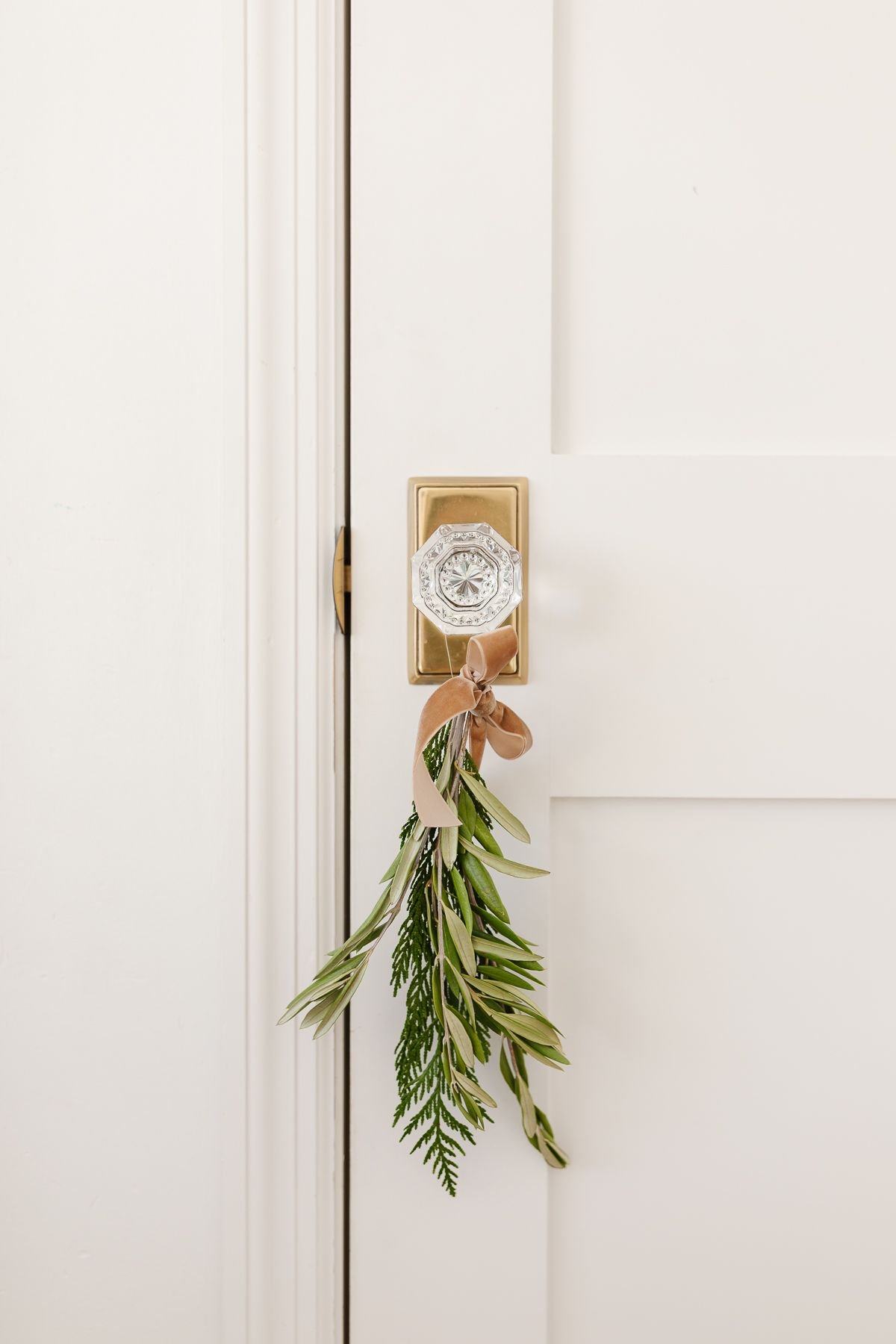 Fresh Christmas greenery tied with a bow onto a glass door knob.