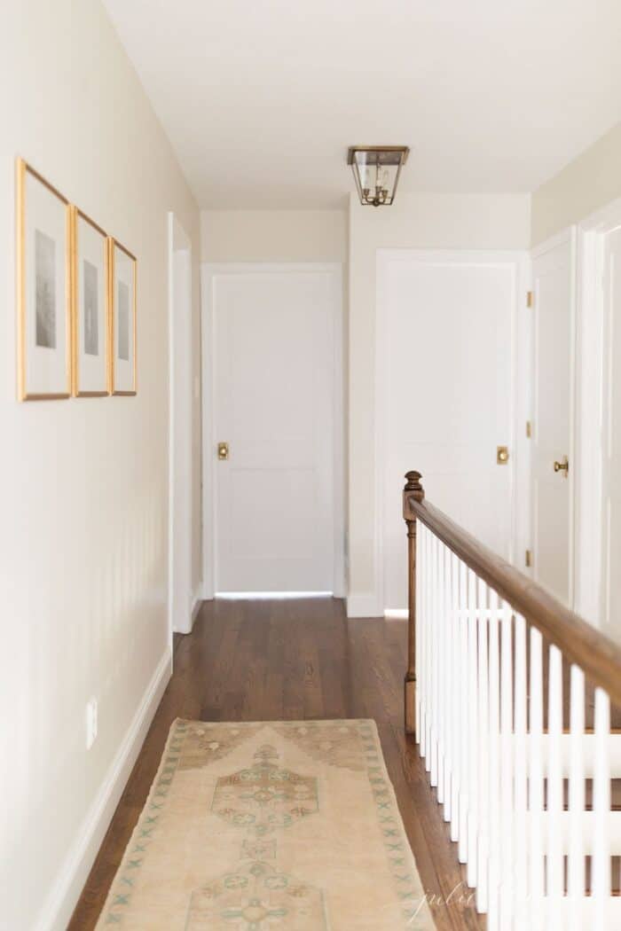 A long hallway in a home, painted white, with brass doorknobs on each wooden door.