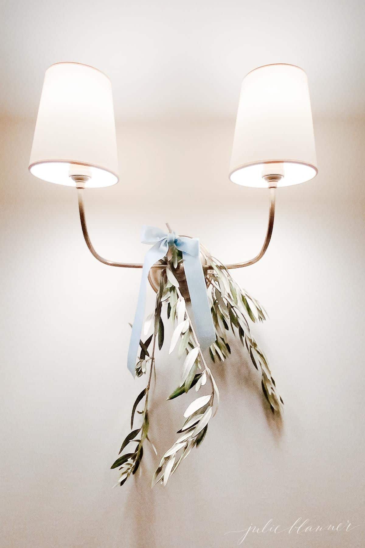 A gold sconce decorated with holiday greens and a blue velvet bow.