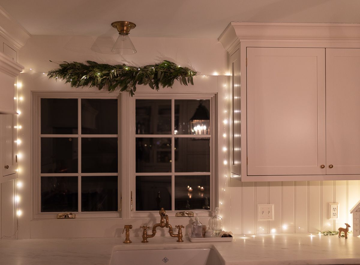 A white kitchen with greenery and lights over the sink