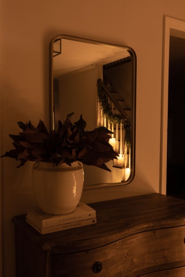 An entry table with a vase of magnolia and christmas lights in the background.