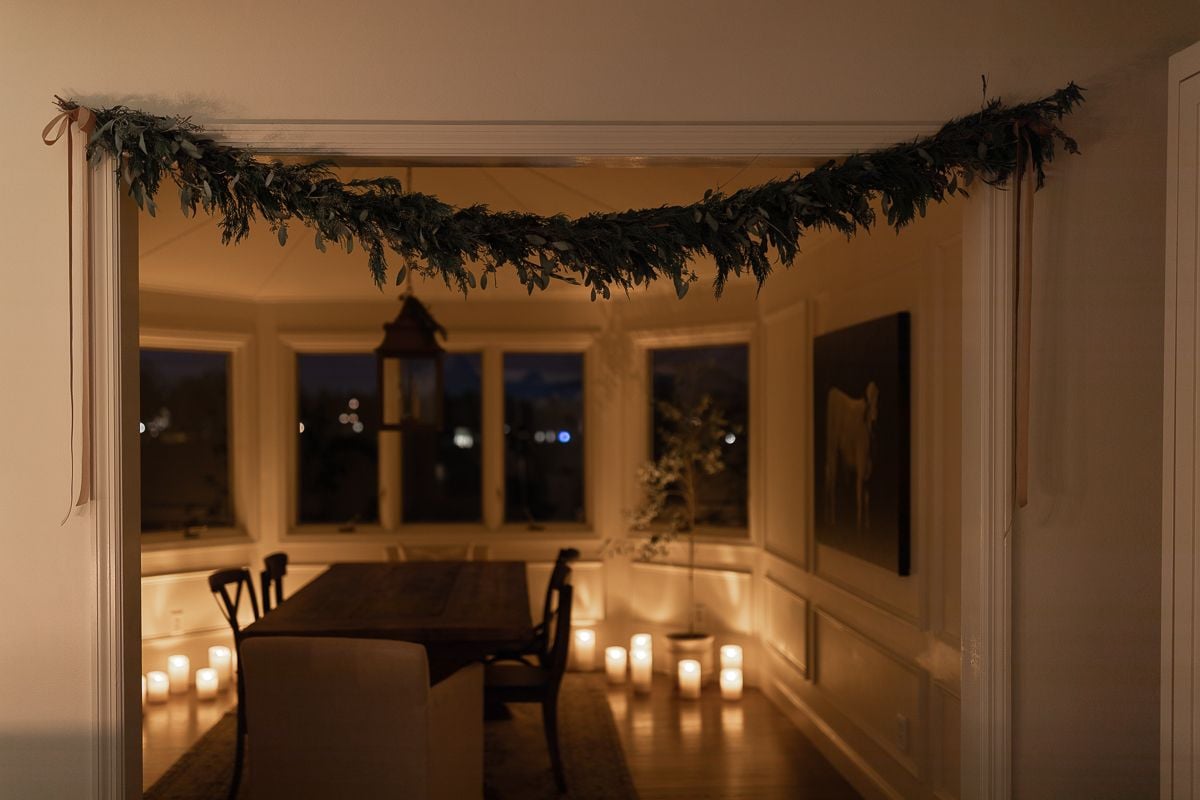 A dining room with candle light and a garland hanging over the doorway for Christmas