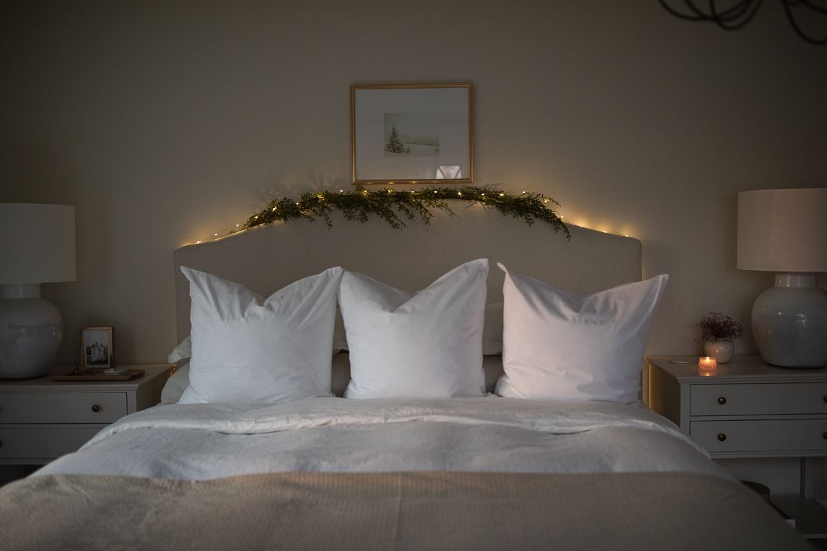 A white bed with a garland and lights over it for Christmas.