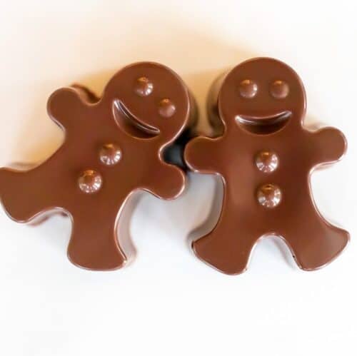 A pair of dark chocolate hot chocolate bombs shaped as gingerbread men on a white marble surface.