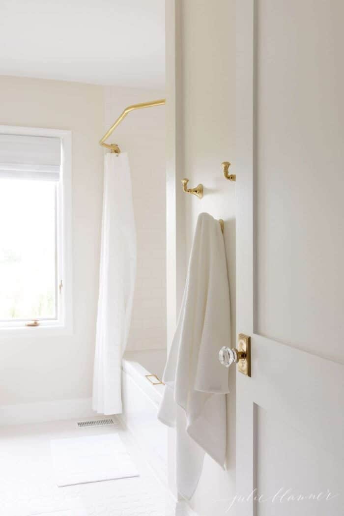 Looking into a white bathroom, with a wooden door featuring a brass and glass door knob.