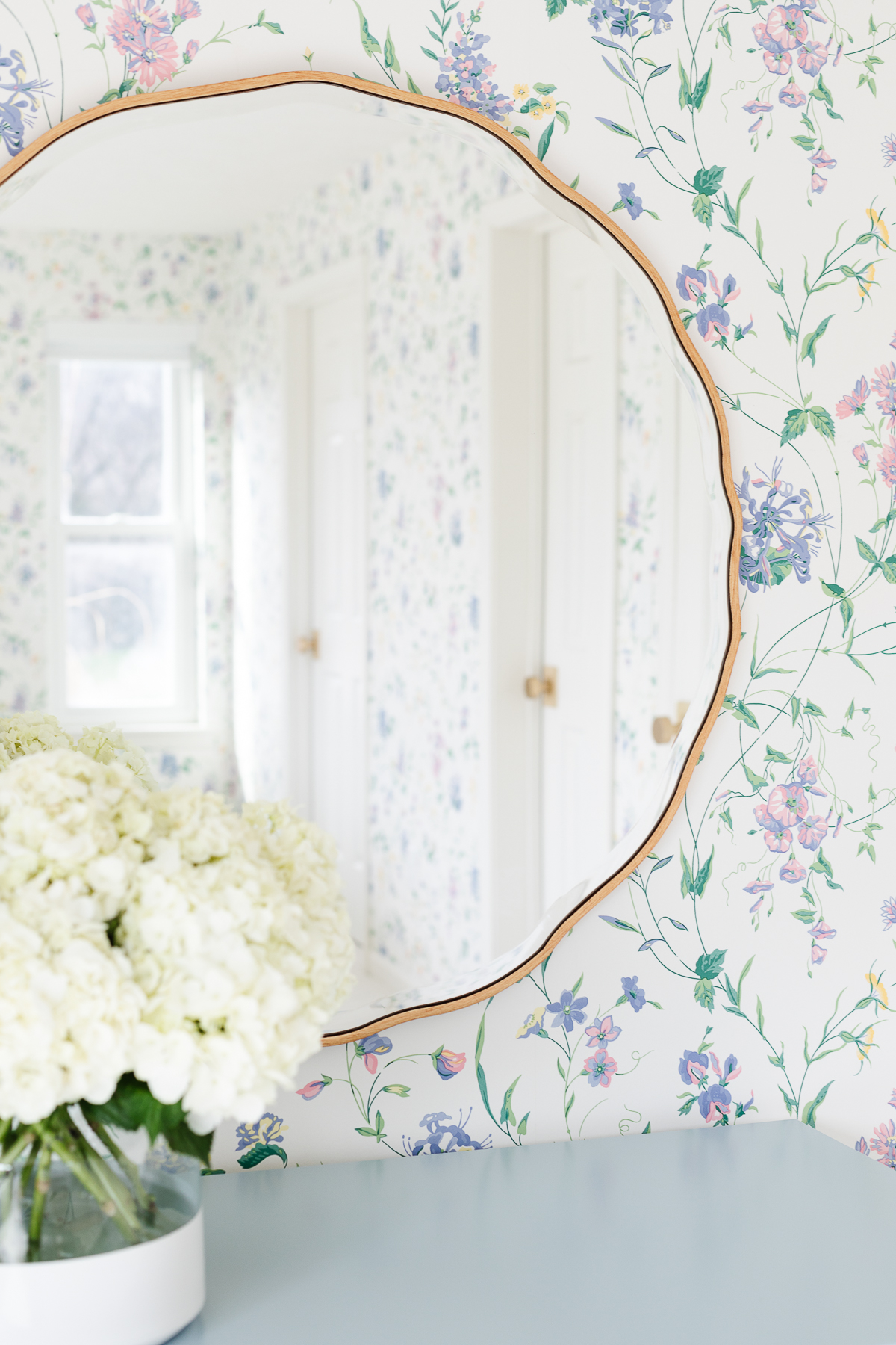 A guest bedroom with a wavy mirror and flowers on top of a blue dresser.