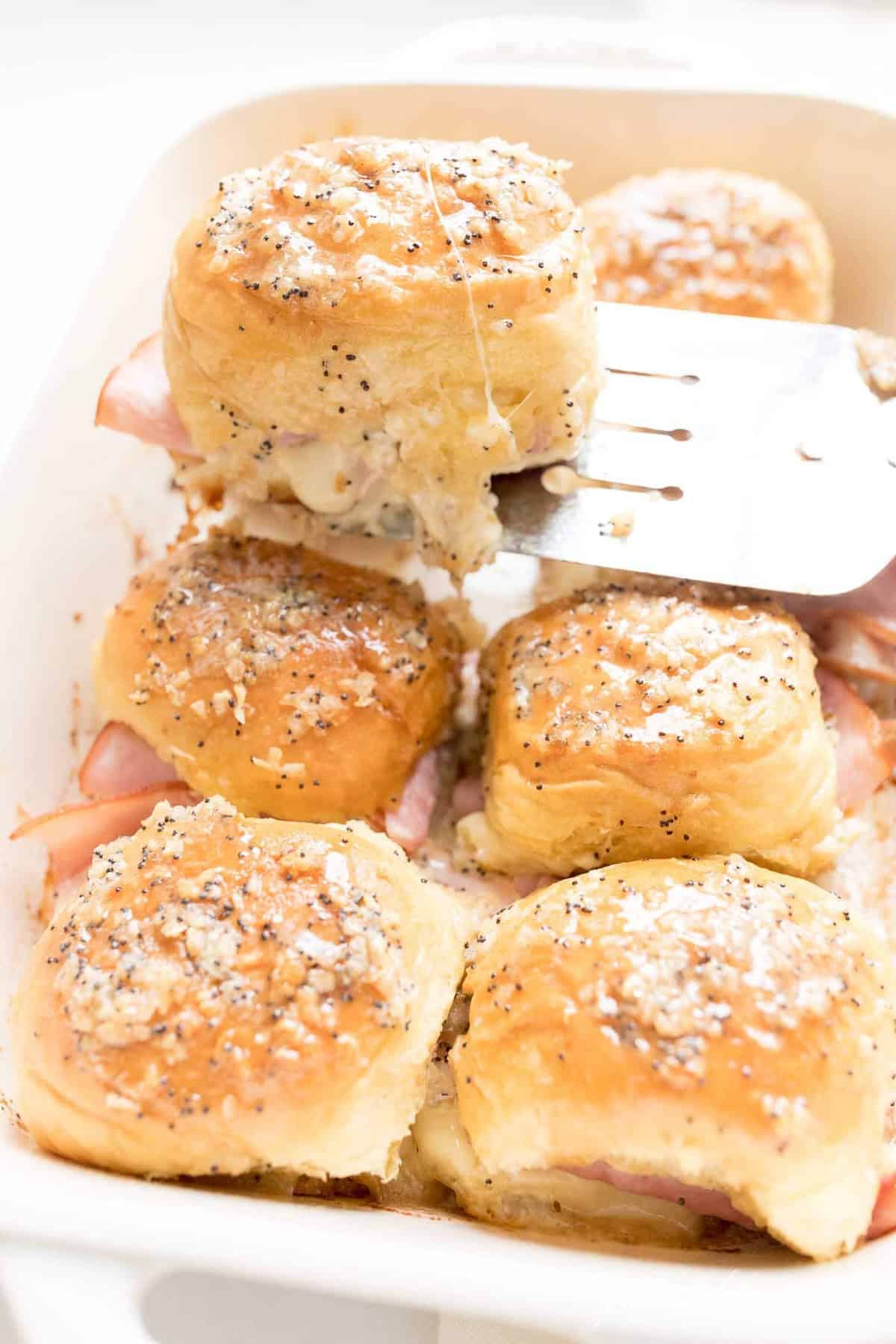 spatula removing ham and cheese slider from casserole dish