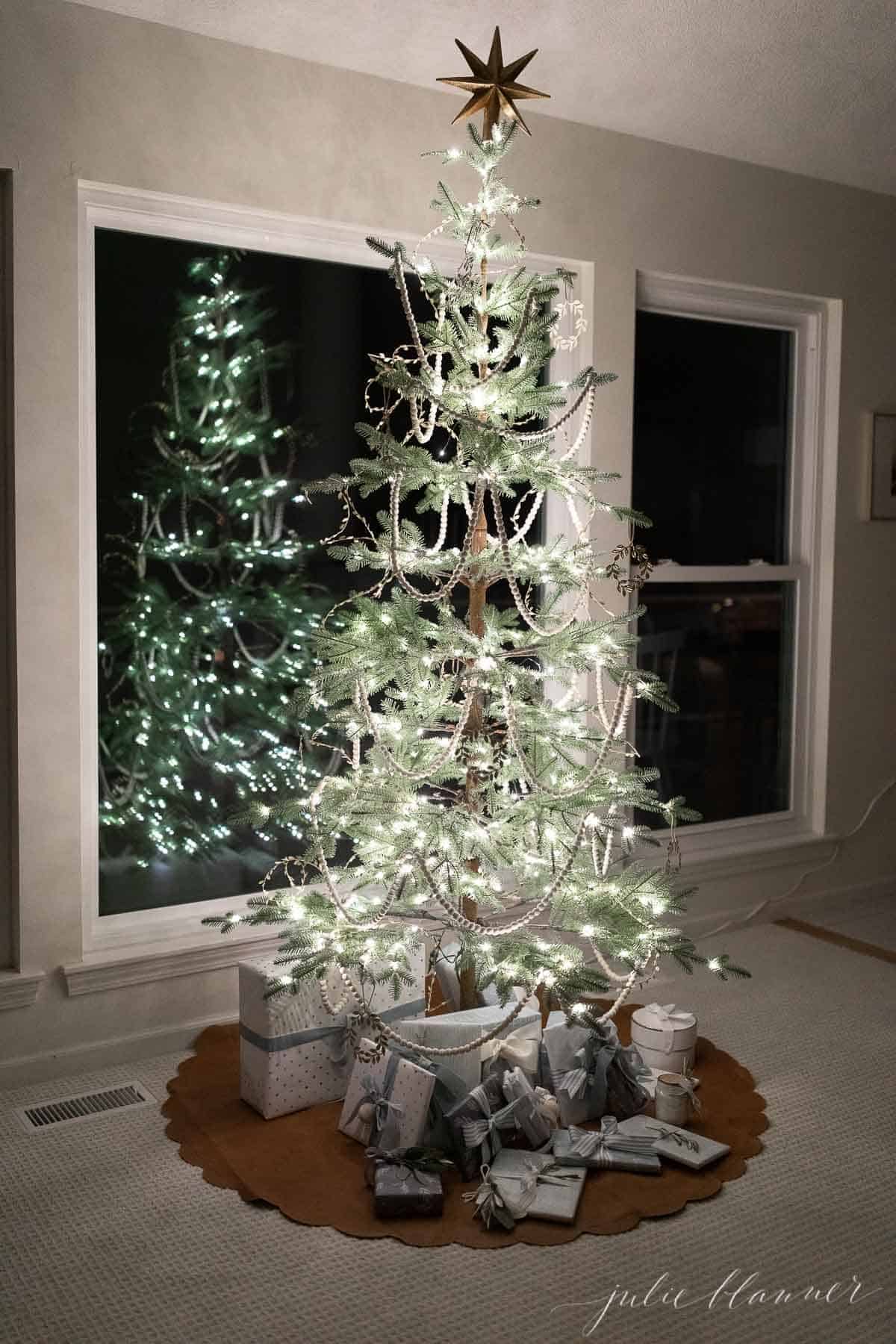 A sparsely decorated Scandinavian inspired Christmas tree reflecting in a window.