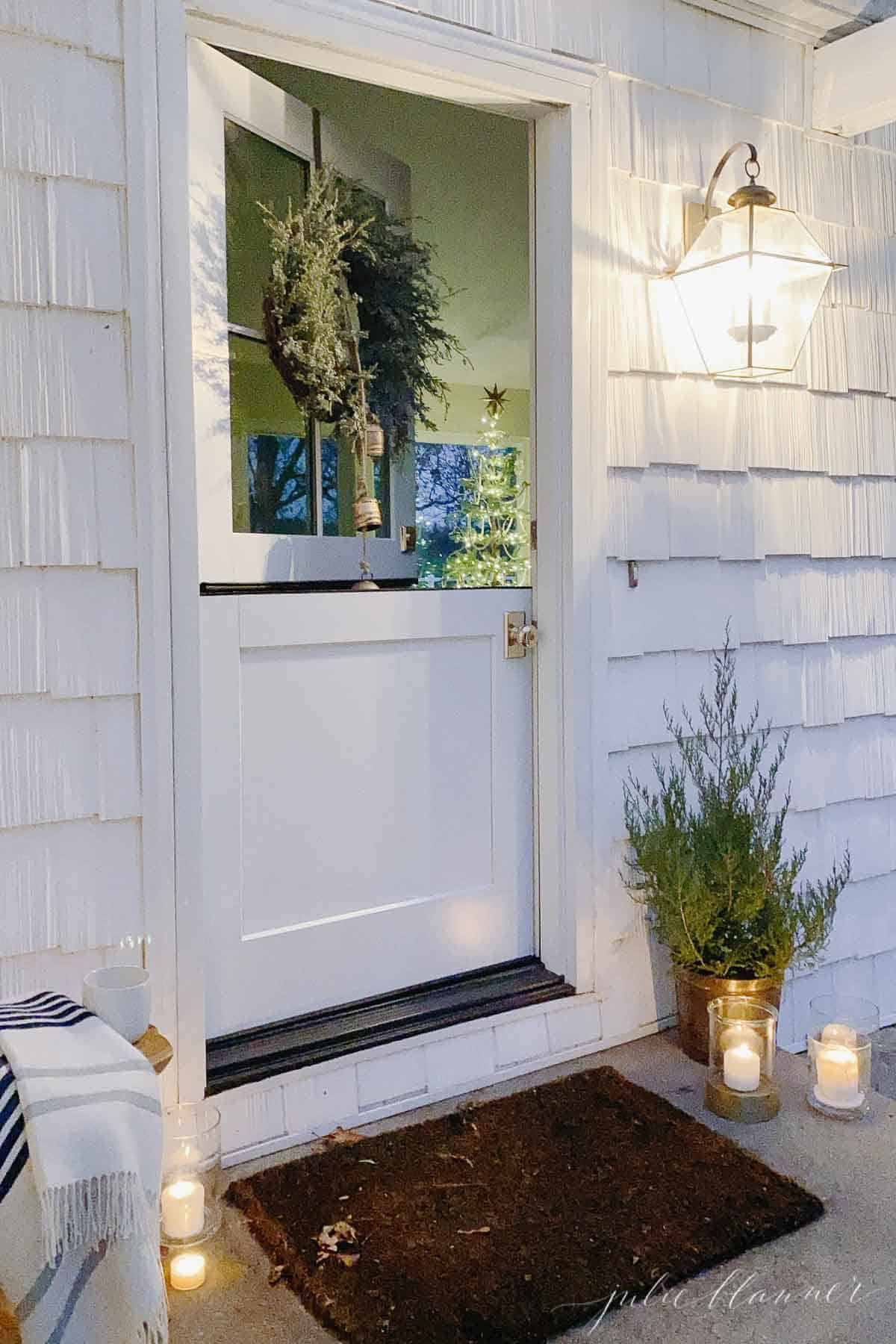 A dutch door on a white cottage decorated with candles and a mini cedar tree for Christmas.
