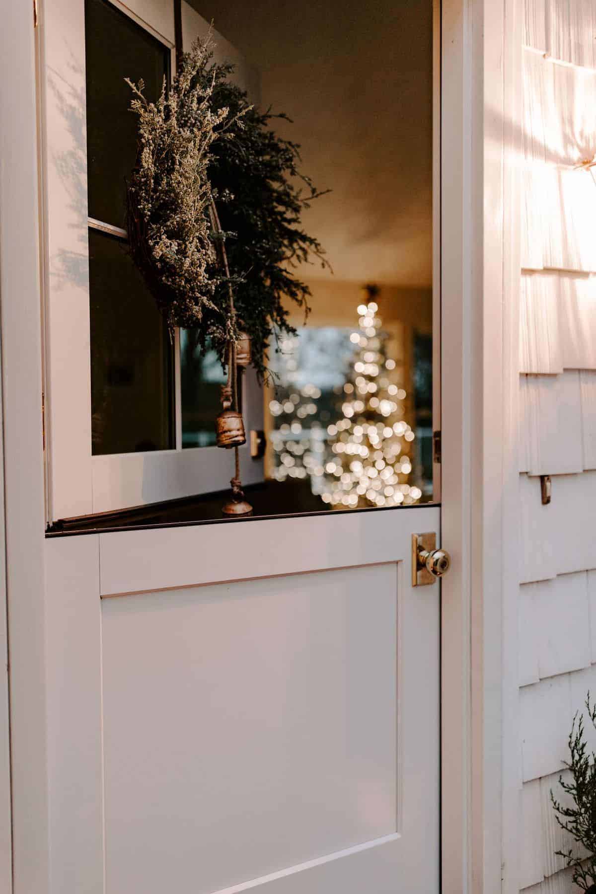 A dutch door on a white cottage decorated with candles and a mini cedar tree for Christmas.