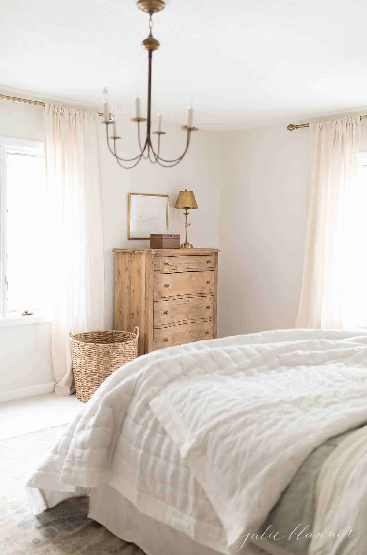 A white bedroom with wooden furniture and a brass chandelier