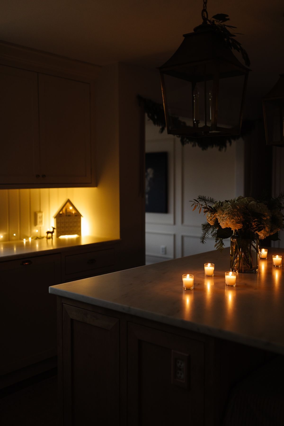 A white kitchen with Christmas flowers and candles on the island at night