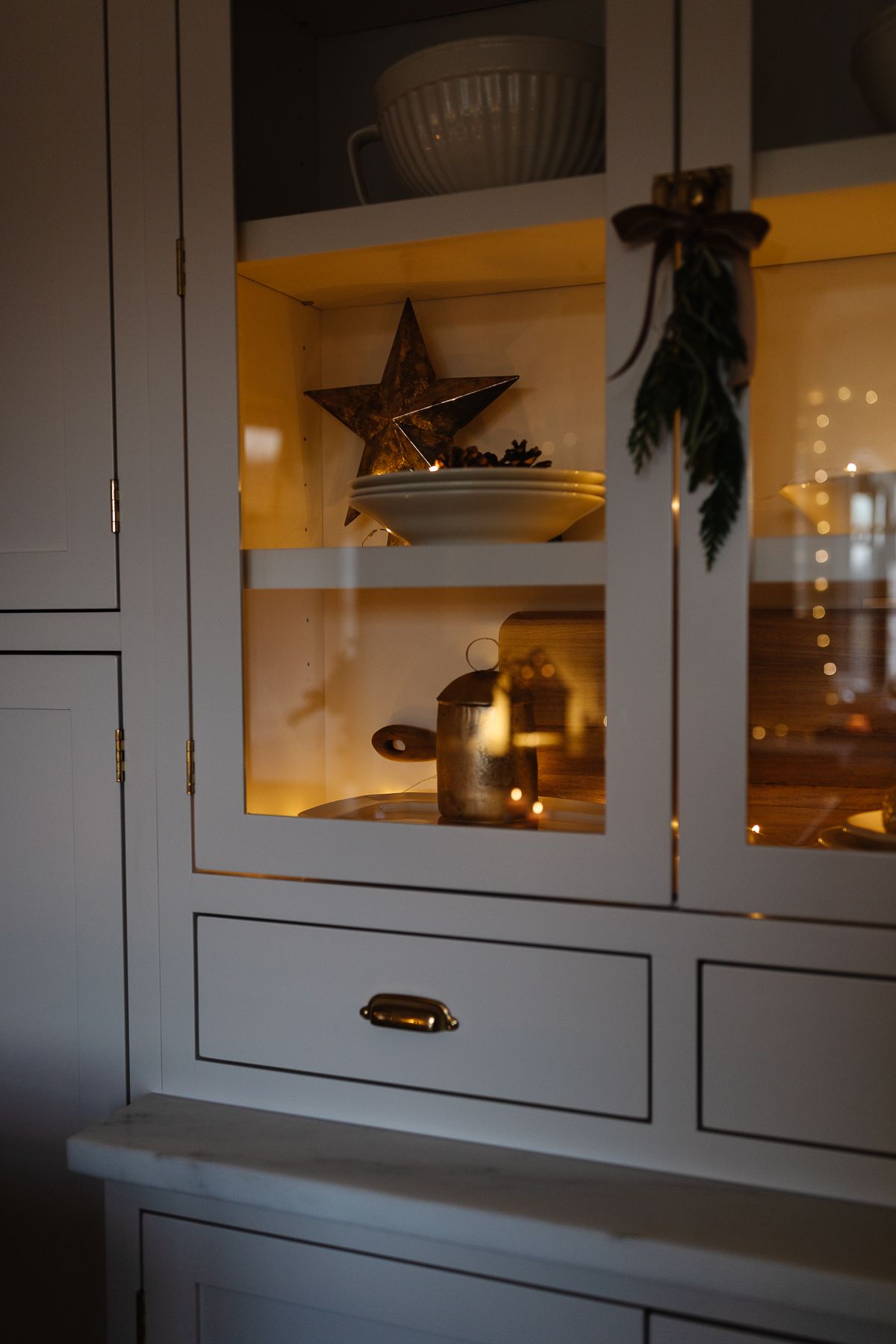 A cabinet in a kitchen with traditional Christmas decorations and lights inside.