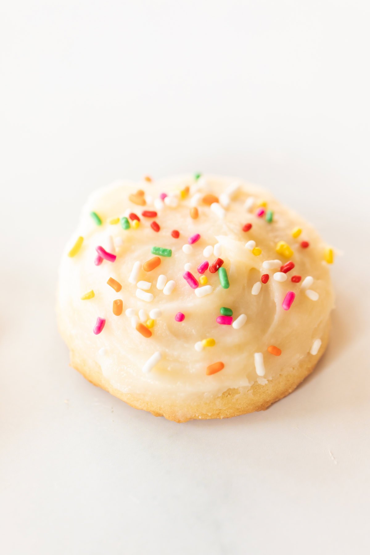 A round, frosted Amish sugar cookie topped with colorful sprinkles on a white background.