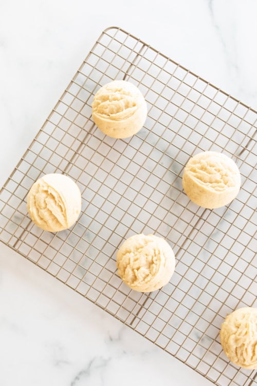 Five Amish sugar cookies cooling on a wire rack over a marble surface.