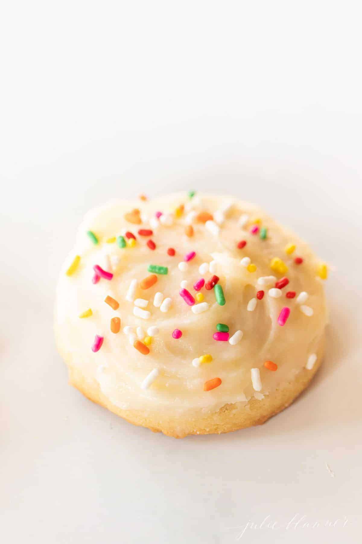 A single melt in your mouth sugar cookie frosted with sprinkles on a marble surface.
