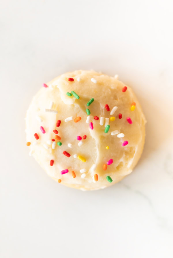 A single round Amish sugar cookie with white frosting and multicolored candy sprinkles, viewed from above on a white background.