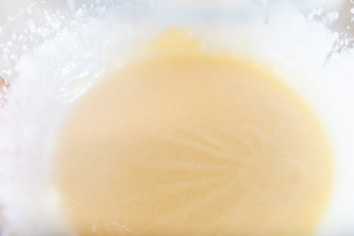 Close-up of a bowl containing a light brown batter with a smooth texture, likely a mixture for baking Amish sugar cookies.