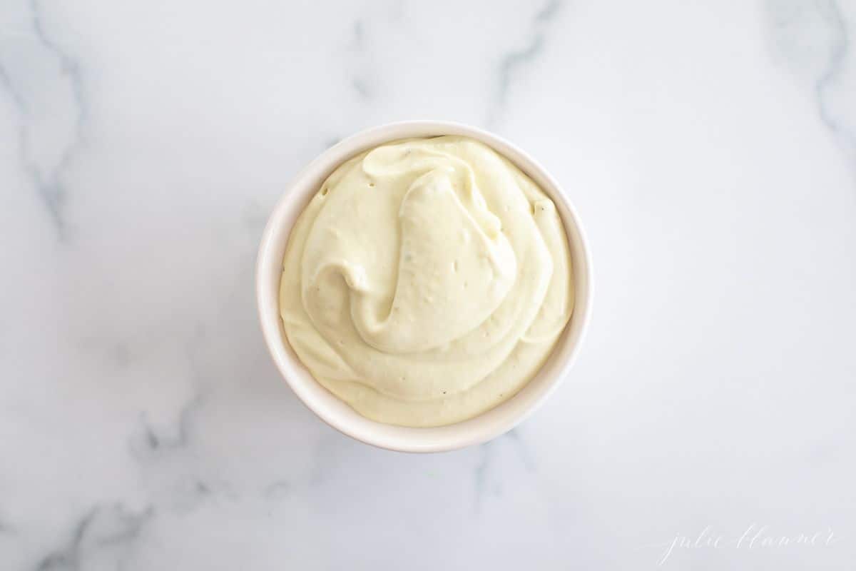 A white ramekin filled with avocado mayo on a marble surface.