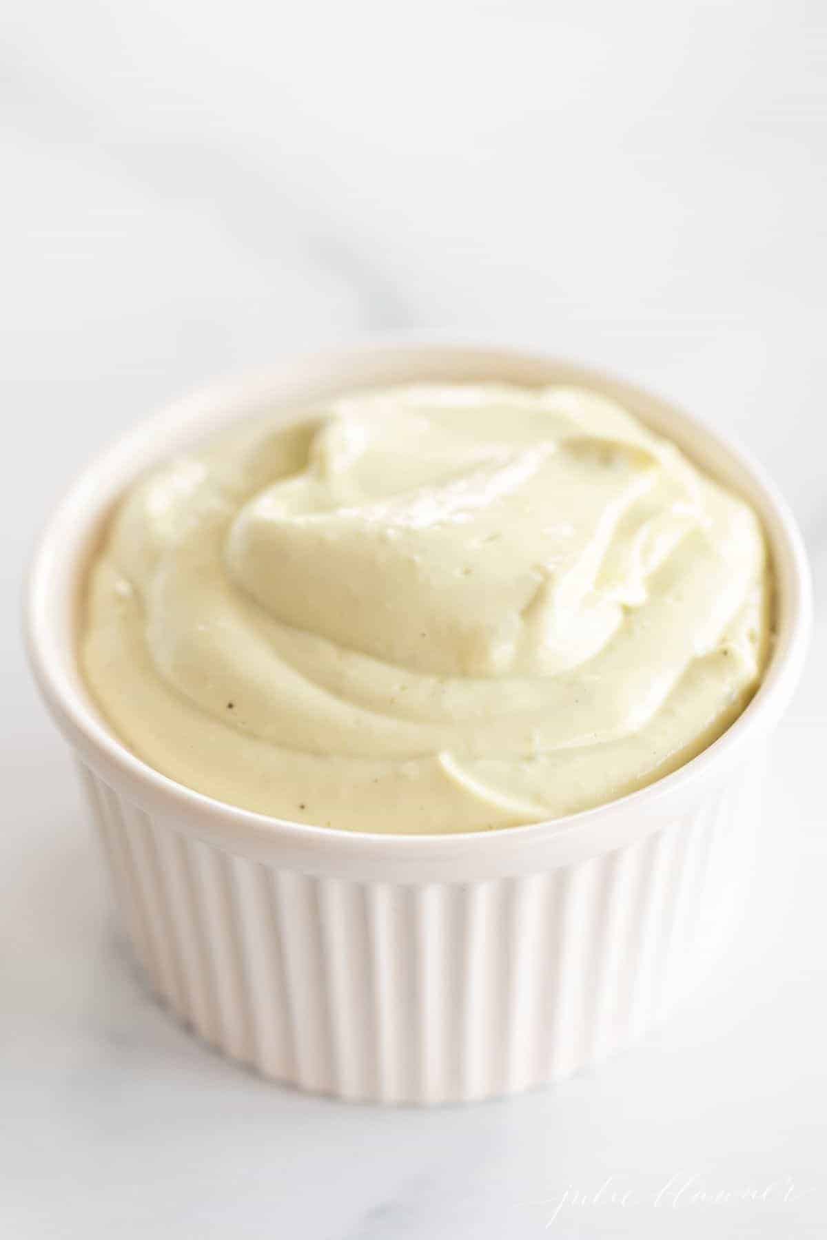 A white ramekin filled with avocado mayo on a marble surface.