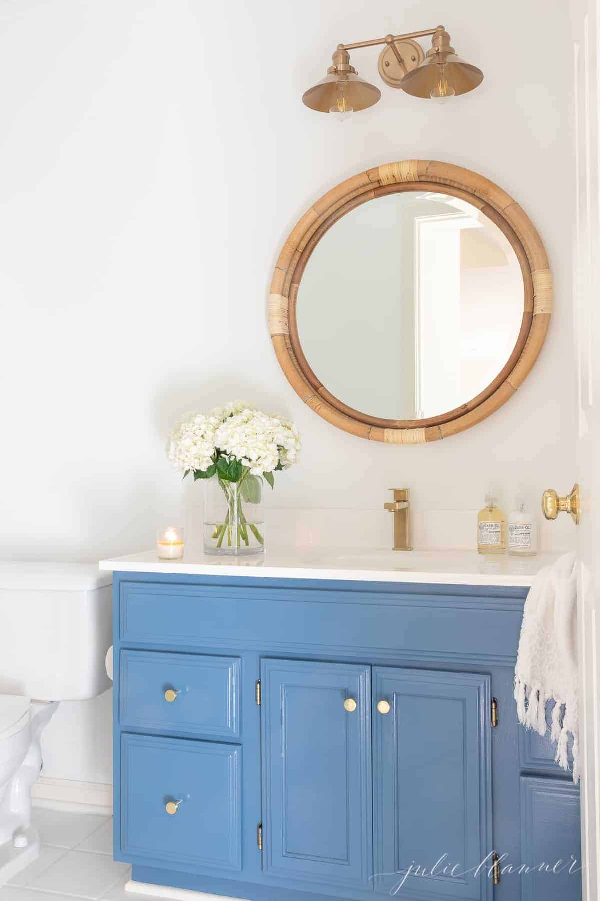 A nautical style bathroom with a blue vanity, gold cabinet door knobs.