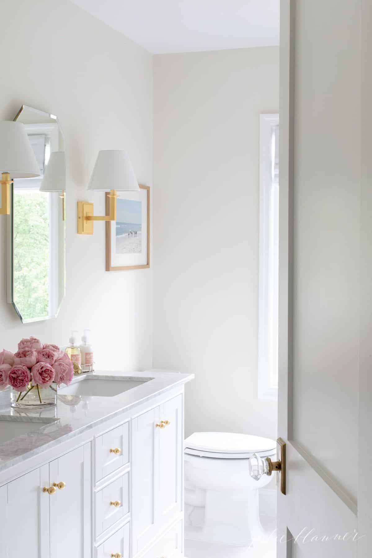 A white vanity cabinet in a bathroom with gold cabinet door knobs.