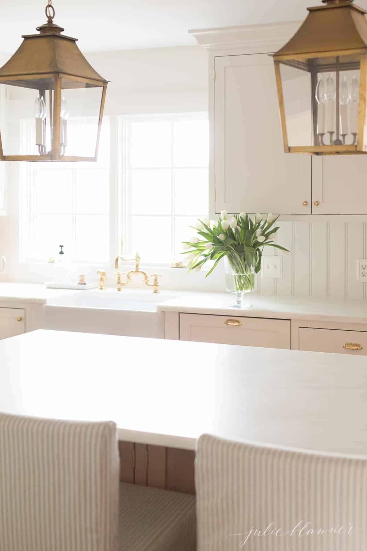 A white kitchen with shaker style cabinets, brass lanterns hanging over island.