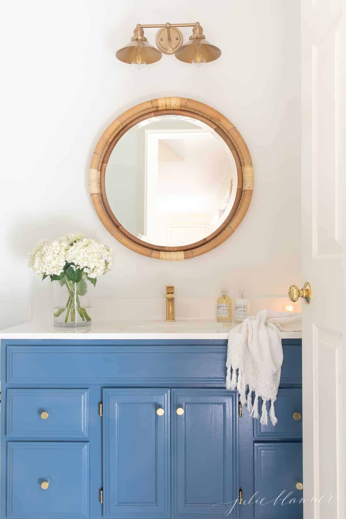 A nautical style bathroom with a blue vanity, gold cabinet door knobs.